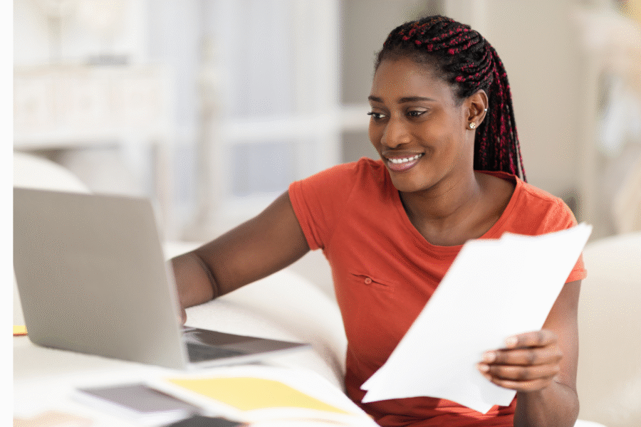 A woman holding paper looking at a laptop